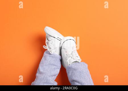 Petit bébé dans des chaussons élégants sur fond orange, vue du dessus. Espace pour le texte Banque D'Images