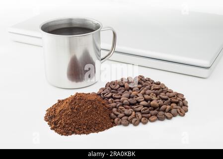 Une tasse de café métallique chaud avec des grains de café, du café soluble instantané et un ordinateur portable Banque D'Images