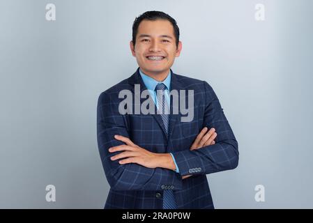 un jeune homme à la peau sombre hispanique réussi sourit avec des bras croisés dans sa veste bleue et cravate, un garçon de bureau, une personne Banque D'Images