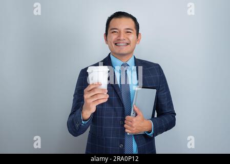 un jeune homme mexicain à la peau foncée sourit tout en tenant une tasse de café et une tablette prêts pour le travail de marketing d'affaires, une personne Banque D'Images