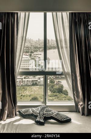 Coussin d'oiseau noir placé sur le coussin de siège à côté de la fenêtre. En regardant par la fenêtre de la chambre, vous pourrez admirer la magnifique vue sur la ville de Bangkok et Chao Phraya Banque D'Images