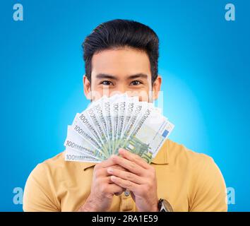 Argent, gagnant et homme couverture face isolée sur fond bleu, studio pour gagner, ventilateur de trésorerie ou prêt financier. Loterie, banque et asiatique personne gagnant Banque D'Images