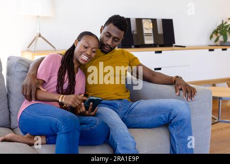 Heureux couple afro-américain utilisant smartphone dans le salon Banque D'Images