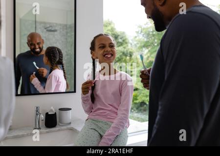 Heureux père biracial et fille se brossant les dents ensemble dans la salle de bain le matin Banque D'Images