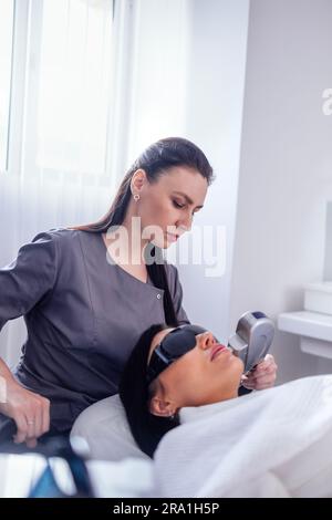 Portrait d'une jeune femme détendue recevant un massage de soulèvement du visage par ultrasons SMAS avec équipement professionnel dans le centre de beauté Banque D'Images