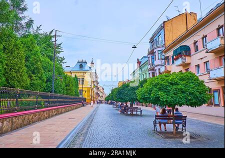 CHERNIVTSI, UKRAINE - 16 JUILLET 2021 : les petites pommes vertes et les bancs à l'ombre, situés sur la rue Olha Kobylyanska dans la vieille ville, sur 16 juillet dans le canal Banque D'Images