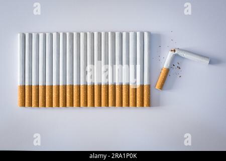 Composition pour exprimer le concept de 'Smoking', de nombreuses cigarettes sont alignées et la dernière est cassée. Banque D'Images