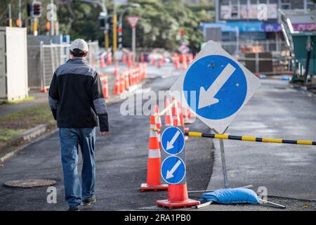 Homme marchant sur la route avec des cônes de circulation orange qui détournent le trafic. Route en cours d'entretien. Auckland. Banque D'Images