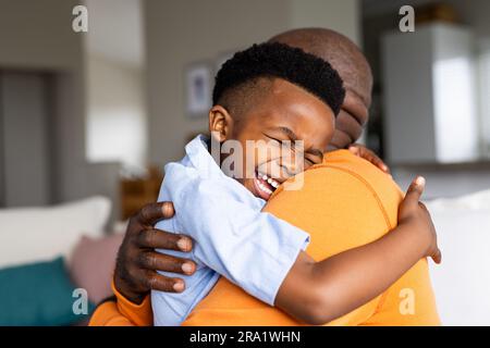 Heureux grand-père et petit-fils afro-américains assis sur le canapé et embrassant Banque D'Images