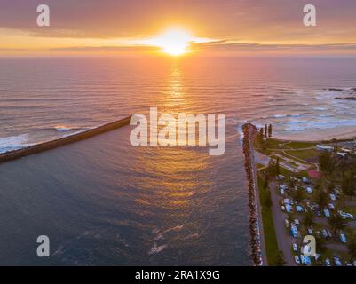 Vue aérienne d'un lever de soleil spectaculaire sur la mer depuis une rivière qui traverse des murs de brise-lames à Port Macquarie, en Nouvelle-Galles du Sud, en Australie. Banque D'Images