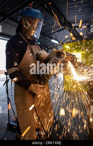 Image rapprochée d'un homme portant un équipement de soudage de protection, utilisant un outil de meulage pour former un morceau de métal émettant des étincelles Banque D'Images