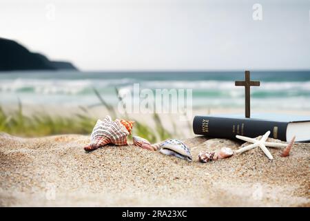 Concept de retraite d'été d'église avec livre de bible, croix de Jésus-Christ et coquillages, conch et étoiles de mer sur la plage de sable et la mer avec vagues Bible d'été sch Banque D'Images