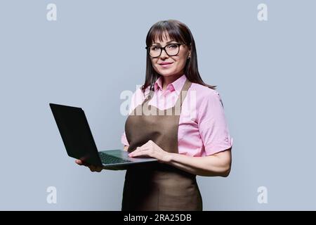 Portrait d'une femme travailleuse avec un ordinateur portable dans les mains sur fond gris Banque D'Images
