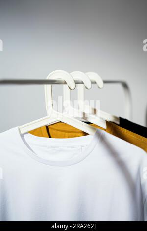 Maquette de t-shirt blanc vierge, modèle sur cintre blanc affiché sur un porte-vêtements blanc avec t-shirts jaune et noir Banque D'Images