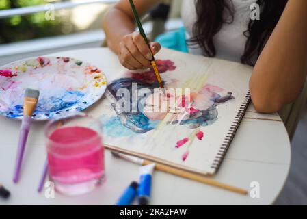 Femme peignant dessin à l'aquarelle de fille asiatique avec pinceau sur une table avec de l'eau et des peintures Banque D'Images