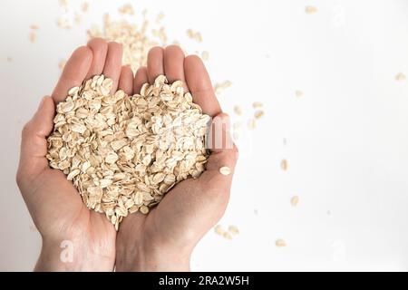 Les mains pleines forment un cœur avec des flocons d'avoine sur fond blanc, image conceptuelle. Super nourriture riche en nutriments et qui peut être utilisé pour plusieurs recettes Banque D'Images