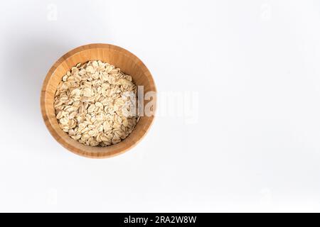 Bol en bois plein de flocons d'avoine sur fond blanc. Super nourriture riche en nutriments et qui peut être utilisé pour plusieurs recettes. Une alimentation saine. Banque D'Images