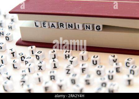 Apprentissage de mots écrit avec des lettres entre un livre pages fond blanc avec des lettres réparties autour de l'éducation lecture concept Banque D'Images