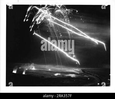 Photographie des fusées éclairantes tirées la nuit avec le placement au sol de l'Artillerie visible. Banque D'Images