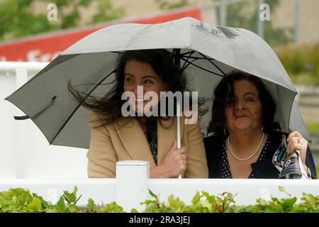 Les spectateurs se réfugient sous un parapluie en raison de la pluie lors de la première journée du festival Dubai Duty Free Irish Derby au champ de courses de Curragh, dans le comté de Kildare. Date de la photo: Vendredi 30 juin 2023. Banque D'Images