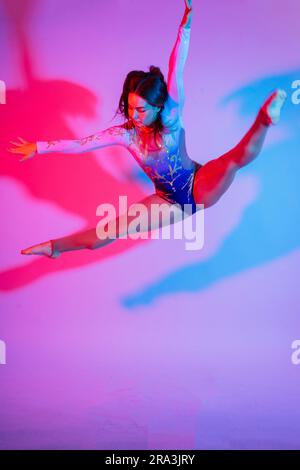 Un gymnaste de fille dans un maillot de bain fait des tours sur un fond blanc et sombre. Vue avant Banque D'Images