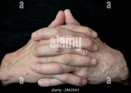 Gros plan des mains d'un homme caucasien pliées en prière sur fond noir Banque D'Images