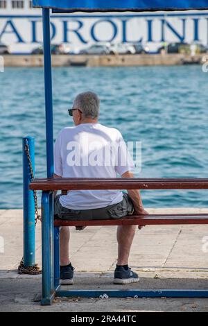 homme d'âge moyen assis sur un banc seul sur le côté du port à split, croatie regardant sur le port aux navires et les événements quotidiens. Banque D'Images