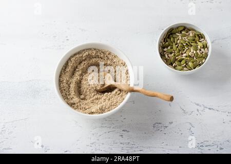 Bol en céramique avec graines de tournesol moulues et un bol avec des graines de citrouille et de tournesol entières sur fond gris clair, vue du dessus. Banque D'Images