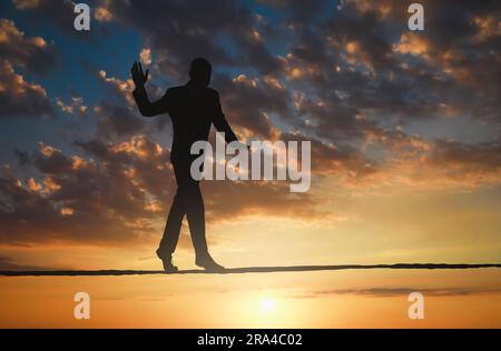 Risques et défis liés à la propriété des activités. Silhouette d'homme en équilibre sur corde dans le ciel du coucher du soleil Banque D'Images