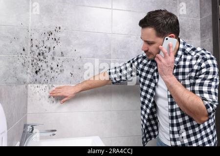 Service de dépose du moule. Homme parlant au téléphone et regardant les murs affectés dans la salle de bains Banque D'Images