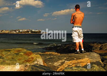 Un jeune adulte se tient au sommet d'une jetée rocheuse le long de la côte à Hampton, New Hampshire, regardant sur les vagues de l'océan et la mer Banque D'Images