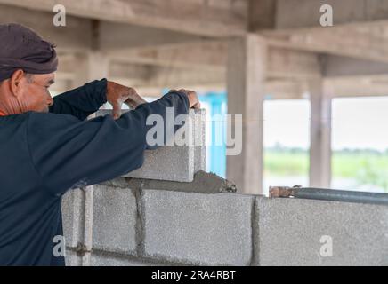 Ouvrier de bricklayer installant de la maçonnerie en brique sur le mur intérieur avec couteau à pâte à truelle dans le chantier de construction. Banque D'Images