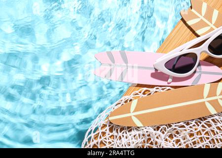 Composition avec mini planches de surf, filet et lunettes de soleil au bord de la piscine Banque D'Images