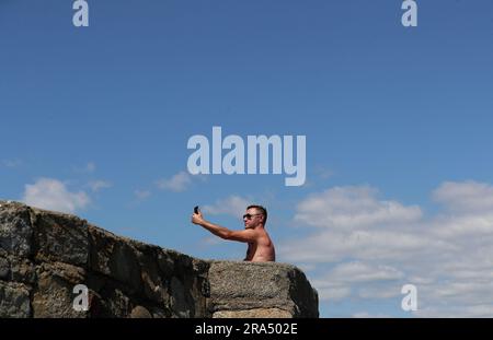 Photo du dossier datée du 16/07/2021 d'un homme prenant un selfie sur le mur de mer de Seapoint à Dublin, le jour d'un été chaud. Une personne moyenne crée 22 tonnes de dioxyde de carbone (CO2) à partir des données qu'elle génère par des photos, des vidéos, des textes et des e-mails chaque année, ce qui équivaut à un vol de Londres à New York 26 fois, selon les scientifiques. Selon les chercheurs, les photos prises sur les smartphones génèrent à elles seules 805 083 C02 tonnes par an, ce qui a une empreinte carbone similaire à celle des vols de Londres à New York 934 109 fois. Date de publication : samedi 1 juillet 2023. Banque D'Images