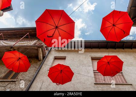 Parasols rouges suspendus au-dessus d'une rue dans le centre historique de Porto Ceresio, Italie Banque D'Images