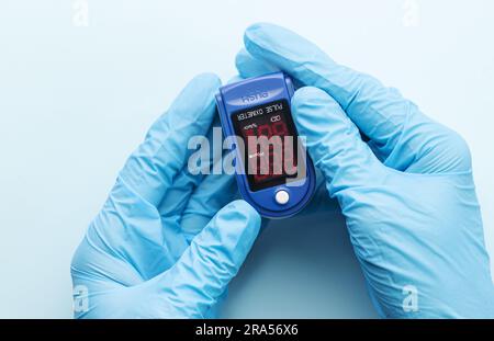 Oxymètre de pouls dans la main du médecin avec un gant sur fond bleu. Une main dans un gant médical tient un dispositif pour le diagnostic de santé Banque D'Images