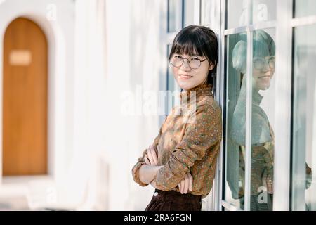 Portrait jeunes lunettes fines souriant femme regardant l'appareil photo bras croisés. Bonne fille debout dans le fond de bureau. Femme d'affaires asiatique réussie standi Banque D'Images