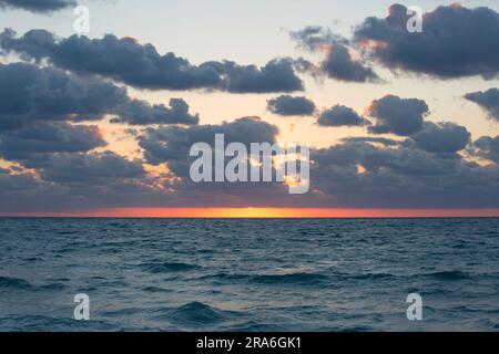 Miami Beach, Floride, États-Unis. Lever de soleil doré sur l'océan Atlantique, soleil partiellement obscurci par les nuages, South Beach. Banque D'Images