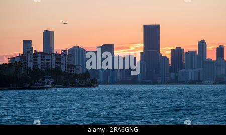 Miami Beach, Floride, États-Unis. Vue de South Pointe Park, South Beach, de l'autre côté de Biscayne Bay au centre-ville de Miami, coucher de soleil, avion approchant de l'aéroport de Miami. Banque D'Images