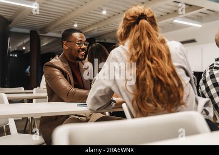 Deux collègues ayant une conversation en classe. Beau homme noir écoutant son collègue de Ginger et souriant Banque D'Images