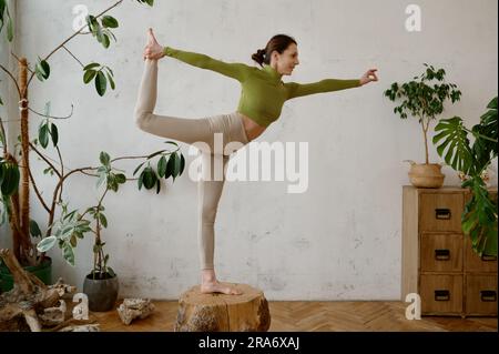 Jeune femme forte en équilibre sur une souche en bois dans la danseuse yoga pose Natarajasana Banque D'Images