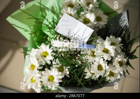 Vue d'en haut d'un magnifique bouquet de fleurs de camomille blanche avec carte de vœux et kit de test de grossesse positif dans le studio de design floral. Happ Banque D'Images