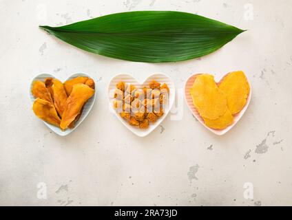 Tranches de mangue séchées et boules dans des assiettes en forme de coeur sur fond clair. Banque D'Images