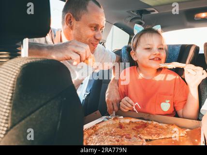 Fille souriante dans le siège de voiture d'enfant tandis que le frein de voyage de voiture de famille arrêter de manger juste cuit pizza italienne avec le père. Des moments heureux en famille, l'enfance, rapide Banque D'Images