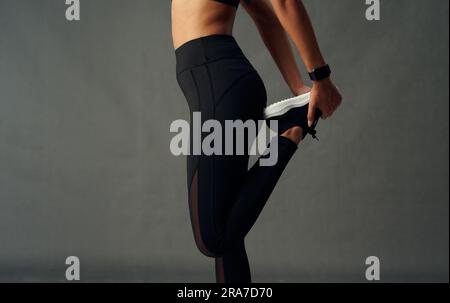 Gros plan de jeune femme biracial portant des leggings avec la jambe relevée pour étirer en studio Banque D'Images