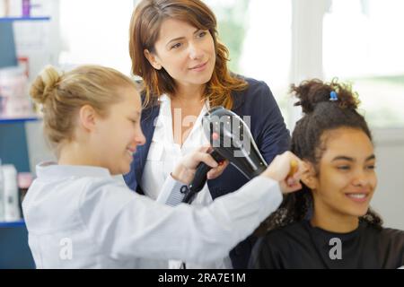 coiffeur stagiaire utilisant un sèche-cheveux sous supervision Banque D'Images