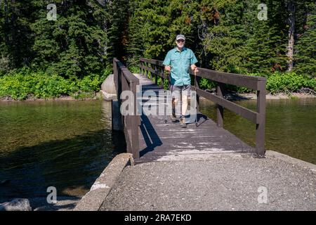 Homme caucasien mûr ne rangeant pas sur un pont traversant une rivière dans une forêt, parc national des Glaciers, Montana Banque D'Images