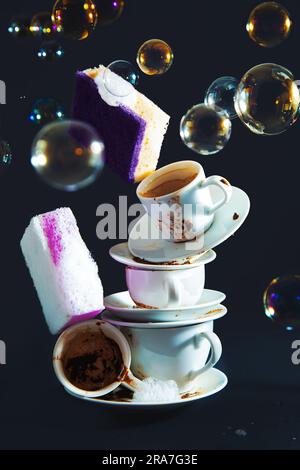 Tasses à café et éponges à vaisselle sales. Fond noir avec bulles de savon. Banque D'Images