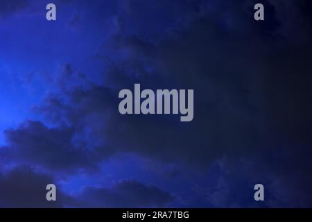 Les nuages se déplacent rapidement à travers le ciel sombre de nuit, les éclairs de lumière de la tempête qui s'approche les éclairent. Banque D'Images
