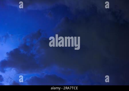 Les nuages se déplacent rapidement à travers le ciel sombre de nuit, les éclairs de lumière de la tempête qui s'approche les éclairent. Banque D'Images